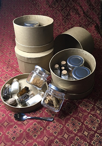 A spice kit including sugar, salt, cinnamon, anise, a nutmeg, pepper, cloves, a small amount of poudre forte, and a small spoon.